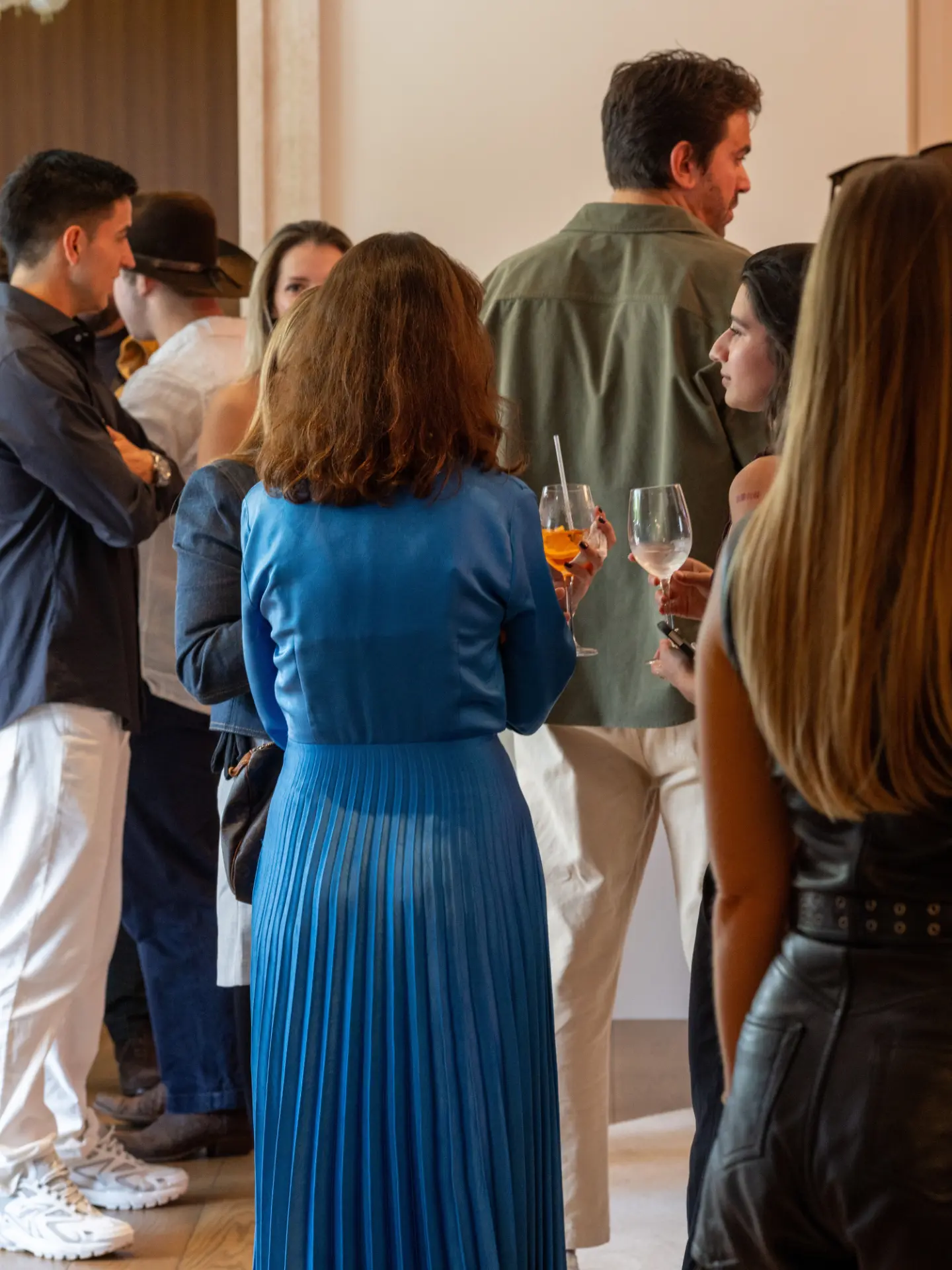 Guests in conversation at a Front Row cultural event, a woman in a blue pleated dress at the centre