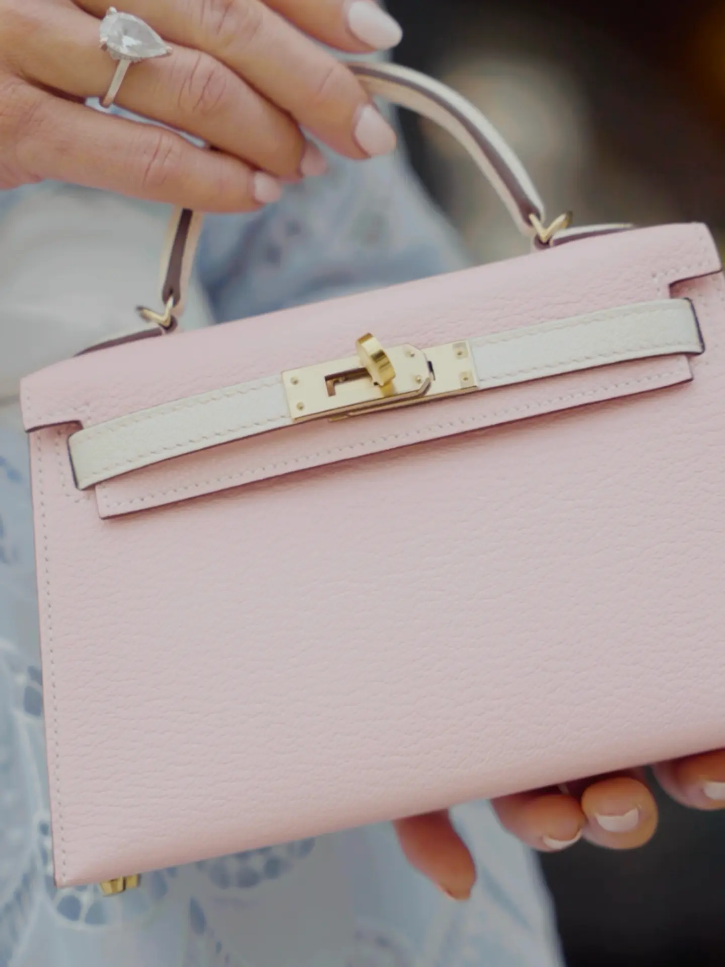 Close-up of a hand holding a pale pink Hermès Mini Kelly with gold hardware