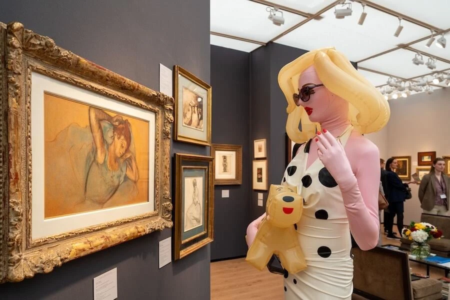 A framed pastel of a resting woman beside an inflatable sculpture of a blonde figure in a polka-dot dress