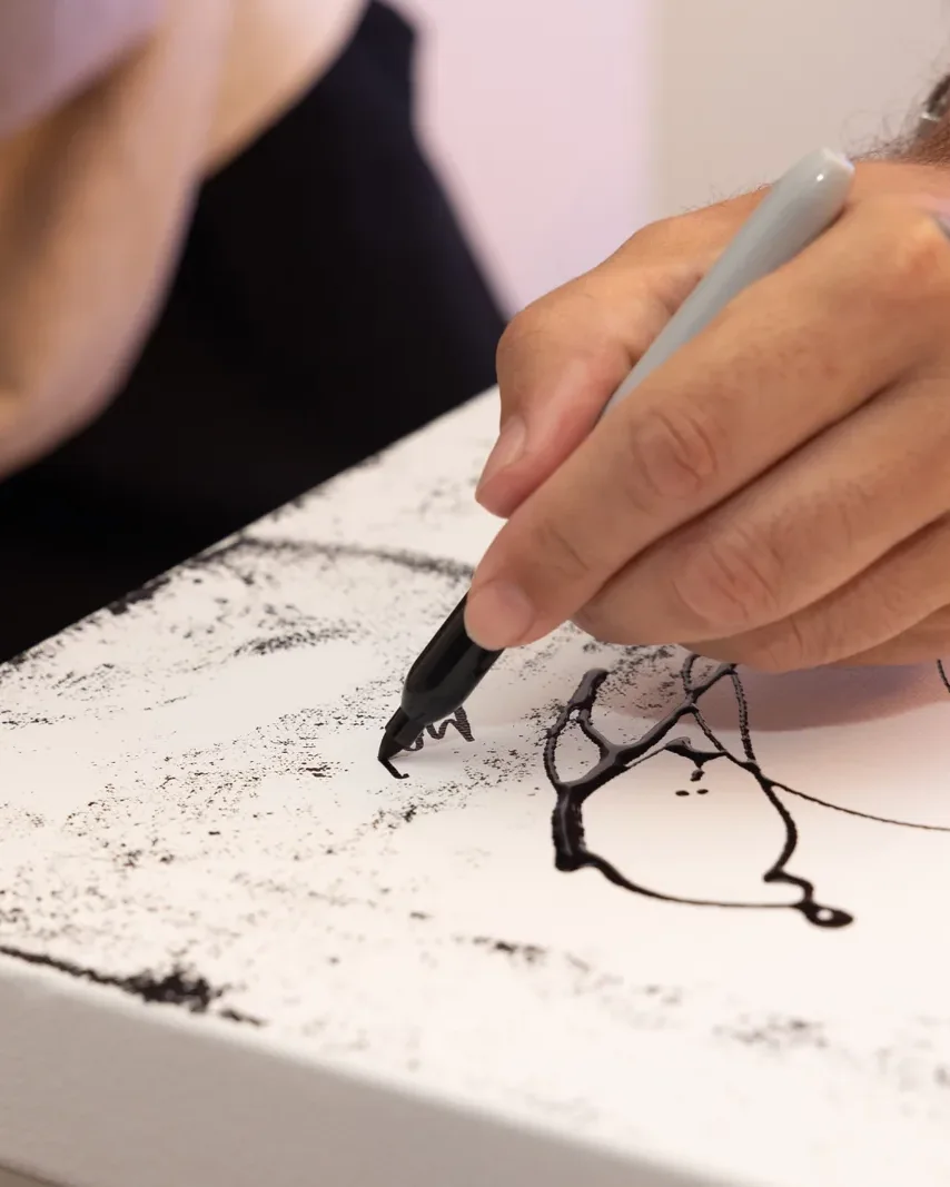An artist drawing in black ink on a white canvas during a live performance at Villa Miami
