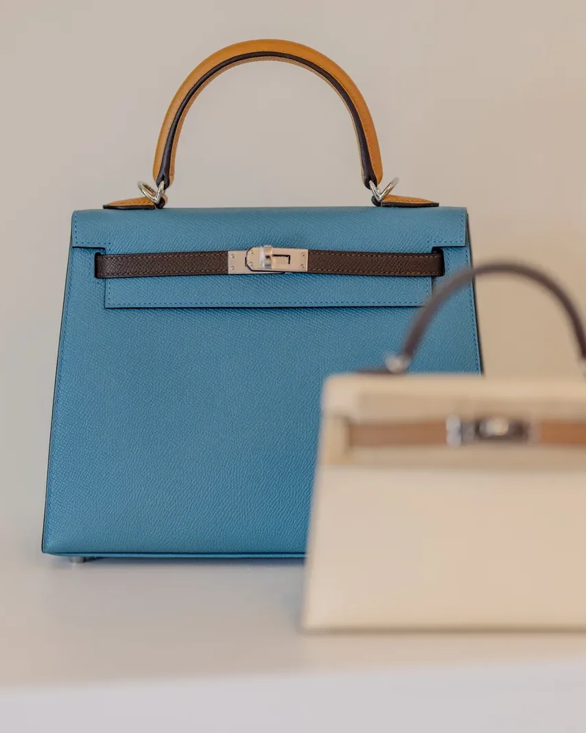 A blue Hermès Kelly and a cream Mini Kelly on a white plinth at Villa Miami